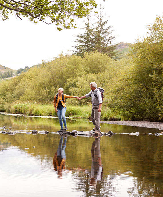 senior couple holding hands while they cross creek in the woods annuity for retirement